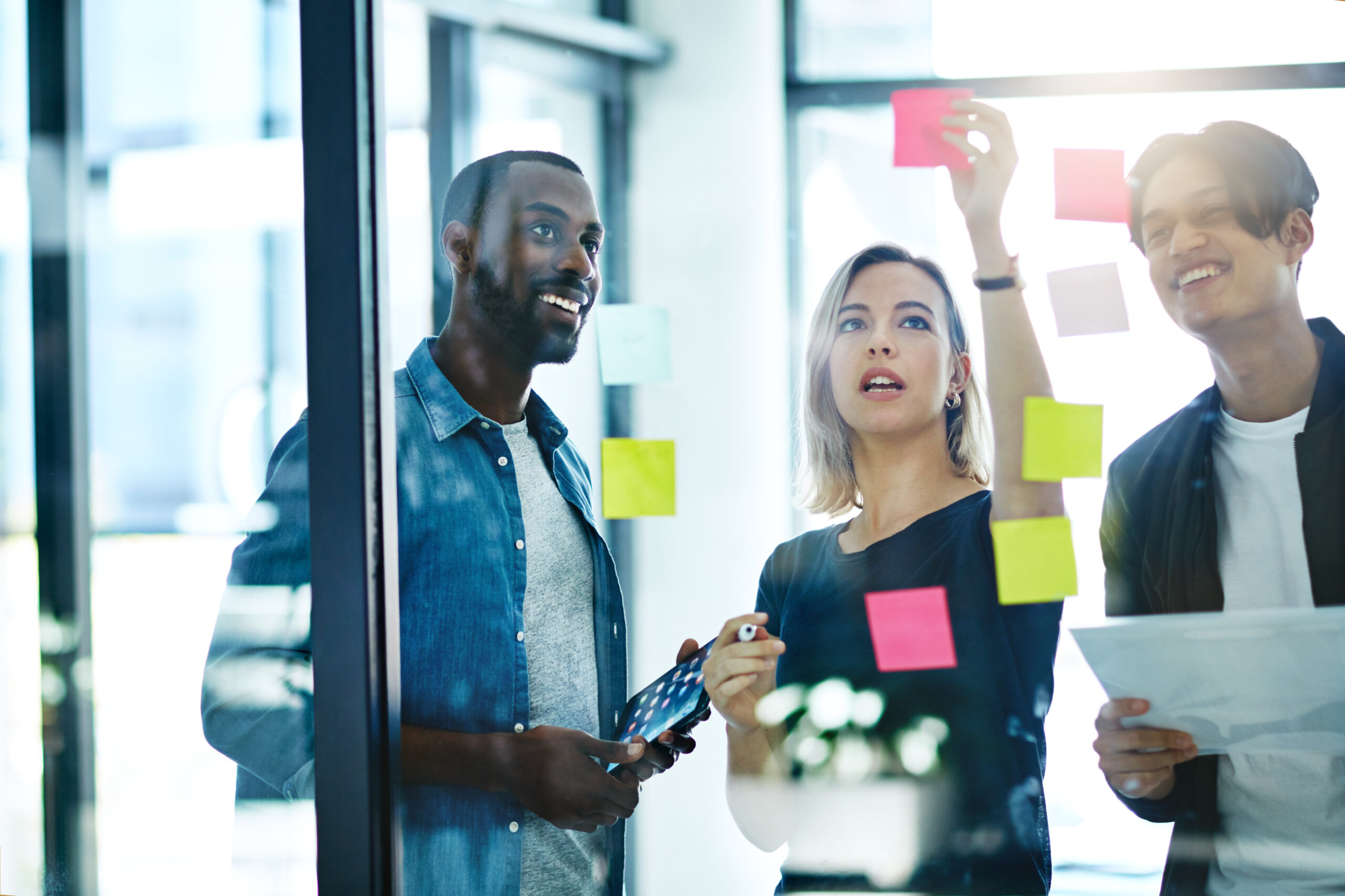 Teamwork, planning and reading sticky notes while brainstorming, talking or sharing ideas. Diverse group of creative businesspeople meeting, training with tablet or paperwork to innovate vision plan